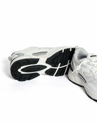 Witte sport schoenen met een gestructureerde mesh bovenkant, zwarte rubberen zool en contrasterende grijze accenten. Heeft een ronde neus en een vetersluiting.