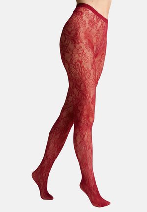 Nogi w przezroczystych czerwonych rajstopach z koronkowym wzorem i kwiatowym motywem, pokazane od talii do palców na jednolitym tle.