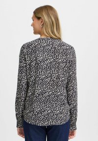 Langärmlige Bluse in Navy mit einem weißen abstrakten Muster, ausgestattet mit einem runden Ausschnitt und Knopfmanschetten, hergestellt aus einem leichten Stoff.