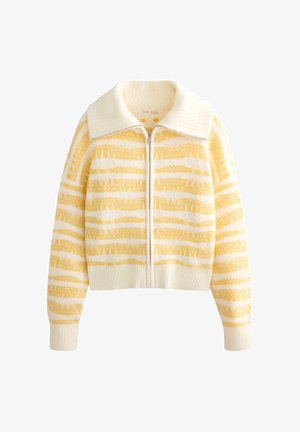 Pleteni jopič z zadrgo, ki ima kremasto belo osnovo z drzno rumenimi vodoravnimi črtami, mehkobo teksture in velik ovratnik.