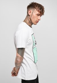 T-shirt bianca in cotone con una grafica di un personaggio dai lunghi orecchi su uno sfondo verde menta. Maniche corte e vestibilità comoda.