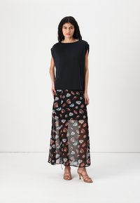 Top scurt negru cu mânecă scurtă, cu un design lejer, asociat cu o fustă neagră fluidă, având un model colorat cu frunze și o textură transparentă.