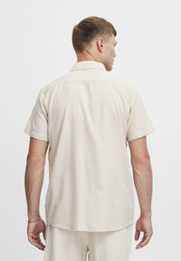 Korte mouw button-up shirt in lichtbeige stof, met een klassieke kraag en een rechte zoom, met zichtbare stiksels aan de randen.