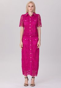 Robe en dentelle fuchsia à manches courtes, avec un boutonnage sur le devant, deux poches poitrine et une longue jupe ajustée ornée d'un motif floral et d'un ourlet.