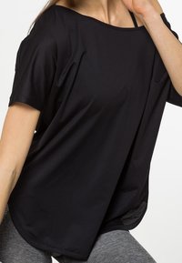 Top negro de corte suelto con mangas cortas, hecho de tela texturizada, con un escote amplio y aberturas laterales para mayor transpirabilidad.