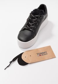 Černé kožené platformové tenisky s umělou kožešinou uvnitř, s černými tkaničkami s logem, bílou gumovou podešví a hnědou visačkou s logem.