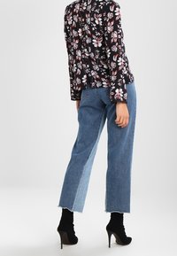 Blouse noire à motif floral avec manches longues, associée à un jean bleu clair taille haute, doté d'ourlets effilochés et d'une coupe décontractée.
