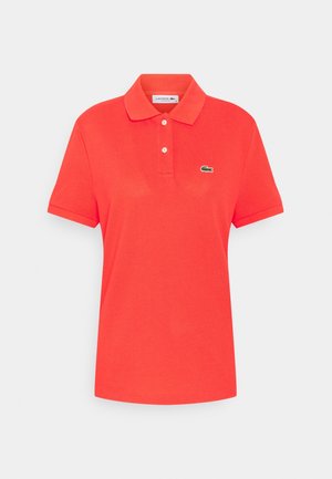 Polo rouge à manches courtes avec un col, deux boutons blancs et un petit logo de crocodile vert sur le côté gauche de la poitrine.
