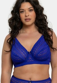 Soutien-gorge en dentelle bleu royal avec un motif géométrique, décolleté en V, bretelles réglables et un nœud décoratif au centre.