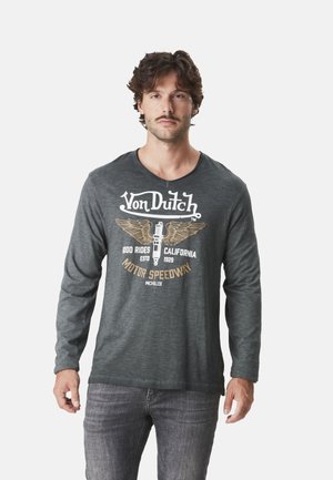 T-shirt gris à manches longues avec un col rond. Présente un graphisme de style vintage en blanc et or, mettant en avant une bougie d'allumage et des ailes.