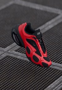 Nike sneaker featuring a bold red and black design, a mesh upper with rubber accents, round shape, and a textured sole for grip.