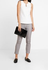 Top bianco senza maniche con dettaglio a chiave, abbinato a pantaloni attillati a quadri. Una borsa a tracolla nera con texture coccodrillo e mocassini completano l'outfit.