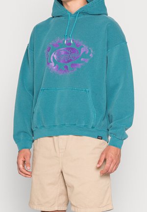 Sudadera con capucha azul verdoso hecha de forro polar, con un gran diseño gráfico púrpura en el centro, bolsillo tipo canguro y capucha ajustable con cordón.