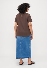 Brown short-sleeve top with a keyhole back detail, paired with a long denim skirt featuring a center seam and frayed hem. Black sandals.