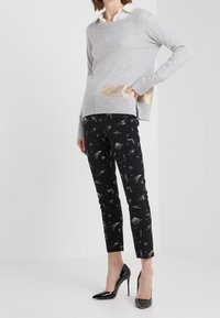 Harmaa neule, jossa on kultainen yksityiskohta taskussa; yhdistetty mustiin housuihin, joissa on avaruusteemainen kuvio, ja mustiin korkokenkiin.