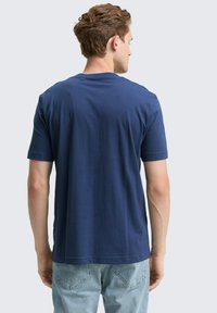 Marineblauwe t-shirt met korte mouwen en ronde hals, gemaakt van zacht materiaal. De achterkant toont een eenvoudig ontwerp zonder patronen of accenten.
