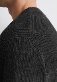 Kohlefarbener gestrickter Pullover mit gerippter Textur, runder Ausschnitt und diagonaler Nahtdetails an der Schulter.