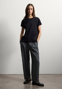 T-shirt nero a maniche corte, dalla vestibilità ampia, abbinata a pantaloni grigi a gamba larga. Mocassini neri, texture liscia, design semplice. Stile minimalista.