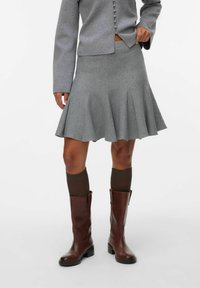 Grå utsvängd kjol med texturerad yta, ihop med en grå knapplös blus och bruna knähöga stövlar, med figursydd midja och plisseringar.