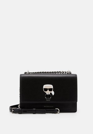 Sac à bandoulière en cuir noir avec une sangle chaîne et une figure de dessin animé représentant une personne portant des lunettes de soleil et un costume sur le rabat avant.