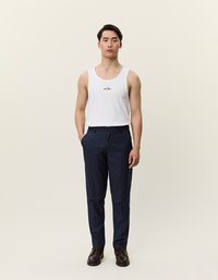 Valkoinen puuvillainen tankkitoppi, jossa on pieni teksti- ja logokuvitus, yhdistettynä merensiniseen housuihin, joiden istuvuus on muotoiltu ja pinta sileä. Ruskeat kengät viimeistelevät asukokonaisuuden.