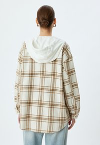 Beige kariertes Flanellhemd mit einer weißen Kapuze. Verfügt über lange Ärmel, einen leicht abgerundeten Saum und Knopfmanschetten.