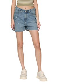 Jasnoniebieskie szorty dżinsowe z przetarciami, postrzępionym dołem i pięcioma kieszeniami. Połączone z beżowymi sneakersami.