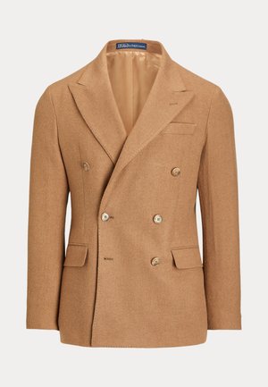 Deux personnes portent des blazers camel à double boutonnage avec des cols roulés gris ; l’une en jean et bottes, l’autre en pantalon gris, mocassins et tenant un sac en cuir.