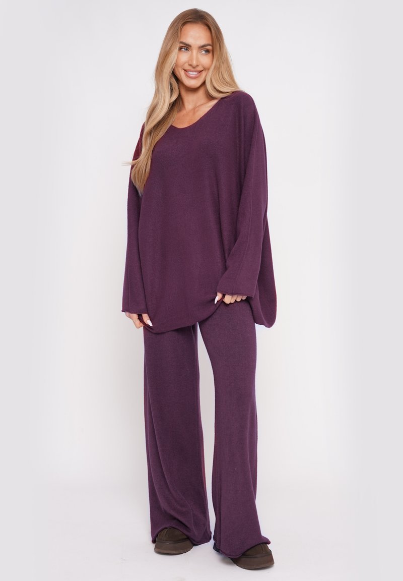 Lila Loungewear-Set mit einem locker geschnittenen Langarmoberteil mit V-Ausschnitt und passenden weit geschnittenen Hosen aus weichem Stoff.