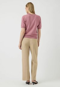 Svijetloružasti kratkosti rukavac s okruglim izrezom, uparen s bež krojenim hlačama ravnog kroja i suptilnom teksturom. Crne cipele.