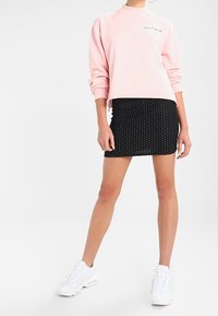 Jasnoróżowa bluza z okrągłym dekoltem, zestawiona z czarną mini spódniczką w kropki. Uzupełniona białymi sneakersami z okrągłymi sznurówkami i grubą podeszwą.