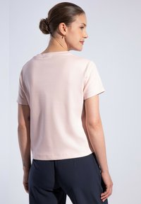 Světle růžové tričko s krátkým rukávem vyrobené z hladkého materiálu, s kulatým výstřihem a standardním střihem. Spodní lem je rovný a dokončený.