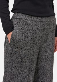 Persona che indossa una maglietta nera a maniche lunghe con una mano nella tasca di pantaloni a righe herringbone bianchi e neri.