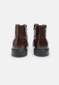 Botas de tobillo de cuero marrón con acabado suave, cremalleras laterales y suela de goma negra texturizada. Forma clásica con un diseño minimalista.