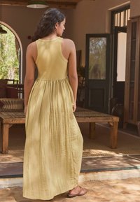 Robe longue, jaune, sans manches, en tissu doux, avec un corsage ajusté et une taille froncée, tombant jusqu'aux chevilles.