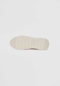 Gumeni potplat Calvin Klein tenisica u boji slonovače. Sadrži teksturirani grip, horizontalne pruge, zaobljeni nos i brendirani detalj. Glatki gumeni materijal.