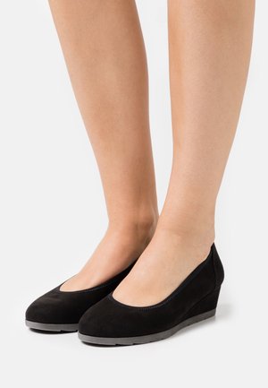 Chaussures à talon compensé en daim noir avec un bout arrondi et un talon solide bas. La tige présente une texture lisse et des coutures simples le long de la bordure.