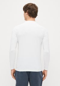 Λευκό μακρυμάνικο T-shirt με απαλό, ελαφρύ ύφασμα. Διαθέτει στρογγυλή λαιμόκοψη και εφαρμοστά μανίκια. Απλός, σύγχρονος σχεδιασμός.