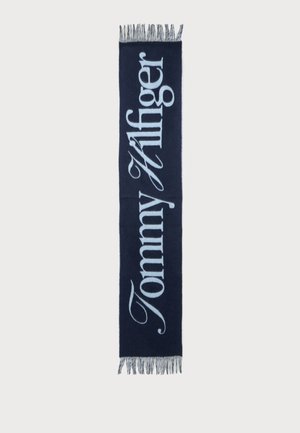 Écharpe bleu marine avec texte "Tommy Hilfiger" bleu clair en écriture verticale et franges aux deux extrémités.