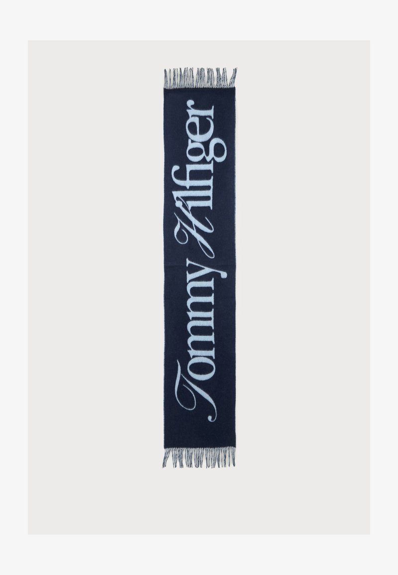 Écharpe bleu marine avec texte "Tommy Hilfiger" bleu clair en écriture verticale et franges aux deux extrémités.