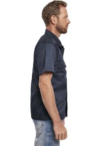 Camicetta a maniche corte di colore navy realizzata in tessuto leggero, con colletto, due tasche sul petto e chiusura a bottoni. Design casual e comodo.