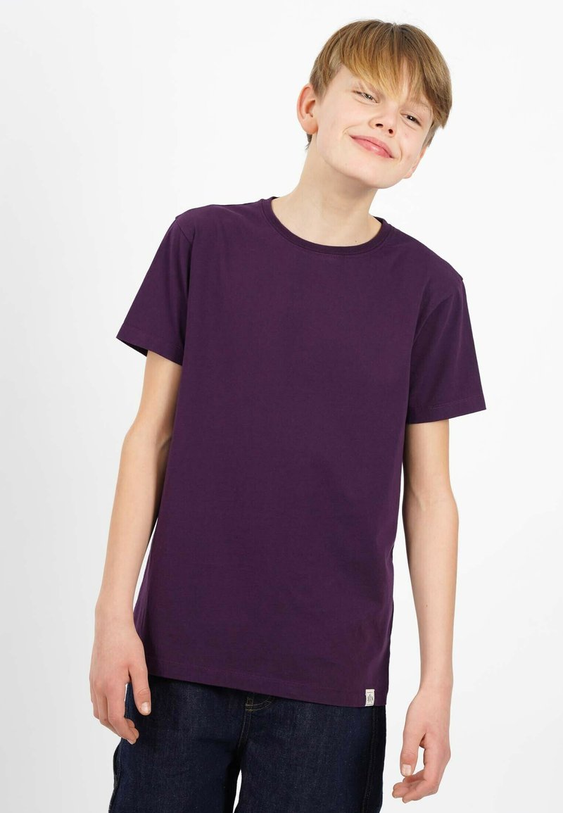 Lila bomullströja med korta ärmar, rund hals och en enkel design. Nederst finns en liten etikett på fållen. Bärs med mörka denimshorts.