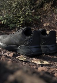 Baskets de sport noires avec un tissu texturé, un design à lacets et une semelle en caoutchouc robuste. Présente un logo de marque déposé et des accents nervurés.