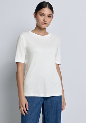 T-shirt en coton blanc avec un col rond et des manches courtes. Le tissu a une texture lisse. Associé à un jean ample bleu.