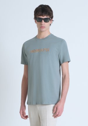 Camiseta de manga corta verde claro con escote redondo. Presenta "MORATO" en un texturizado de animal dorado en el pecho.