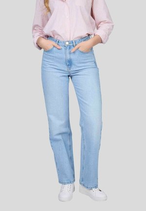 Jean taille haute bleu clair avec une coupe droite, en denim. Modèle portant une chemise à rayures roses et des baskets blanches.