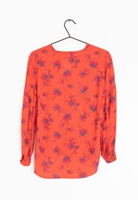 Blouse rouge à manches longues avec un motif floral ; présente des manches froncées, un col rond et un tissu lisse et léger.