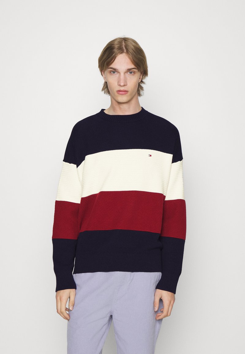 Maglione lavorato a maglia con strisce orizzontali blu navy, bianche e rosse. Texture a coste con scollo rotondo e dettaglio del logo sul petto.