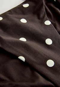 Melnas audums ar lieliem baltajiem punktiņiem, gluda tekstūra un drapēts dizains, kas izceļ maigas krokas un kontūras.