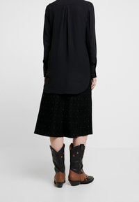 Chemise noire à manches longues avec un dos plissé, associée à une jupe noire plissée avec des lignes verticales. Bottes de cow-boy marron et noires avec des accents étoiles.